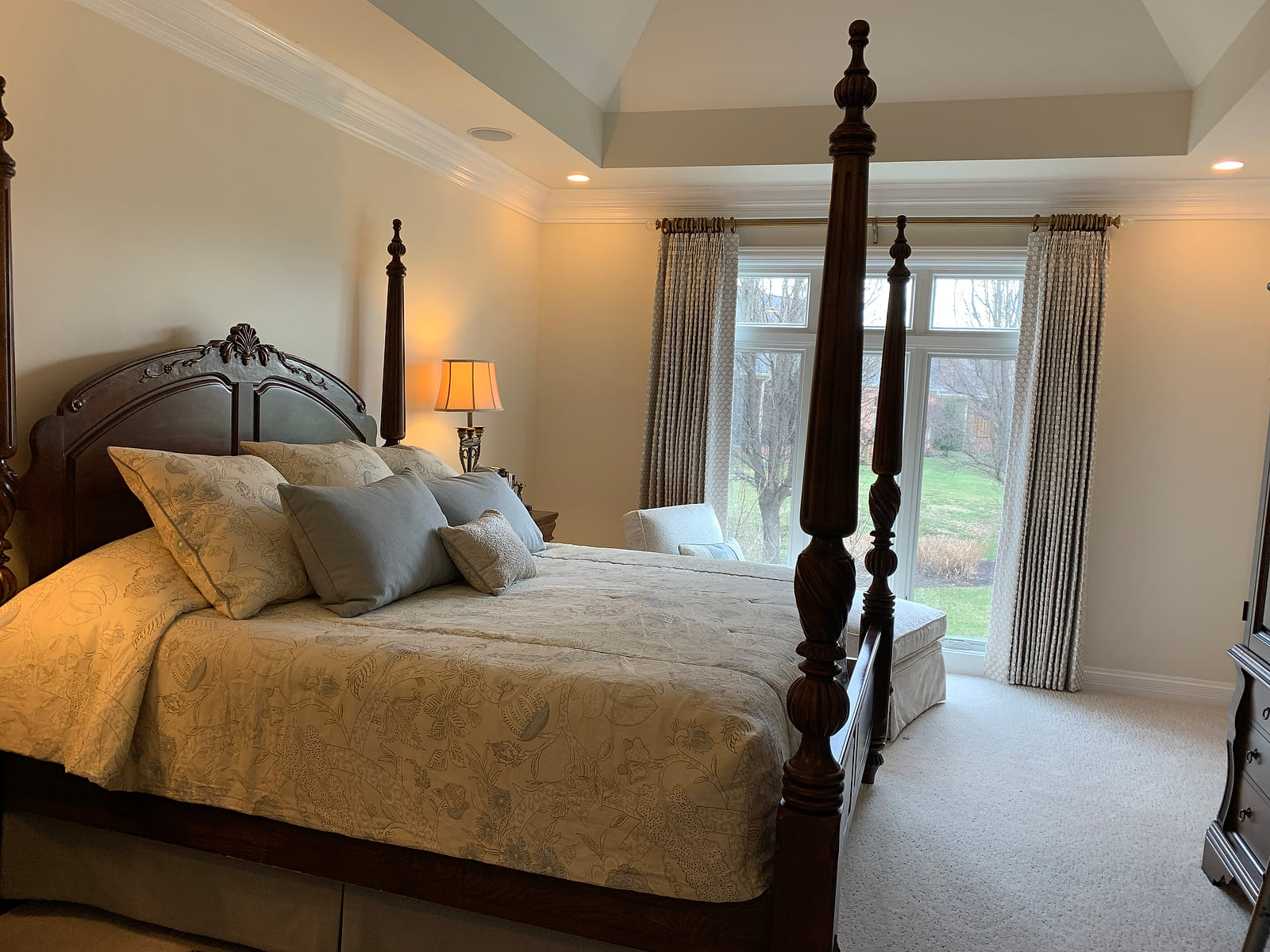 A bedroom with a four-poster bed dressed in custom bedding and full-length draperies at the window