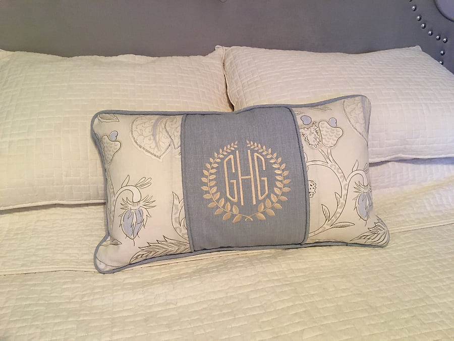 A monogrammed cushion on the bed, embroidered with a wreath and initials